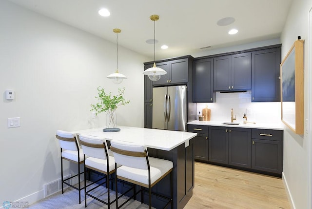 2630 2nd St E, Fargo, ND 58078 - kitchen featuring freestanding refrigerator, a kitchen bar, light countertops, light wood-type flooring, and decorative light fixtures