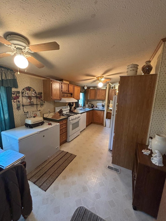 2126 3rd Ave NW Unit 80, Owatonna, MN 55060 - kitchen featuring white appliances, a ceiling fan, wallpapered walls, brown cabinets, and under cabinet range hood