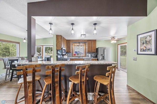 3402 Par St N, Fargo, ND 58102 - kitchen featuring appliances with stainless steel finishes, tasteful backsplash, brown cabinetry, wood finished floors, and a breakfast bar