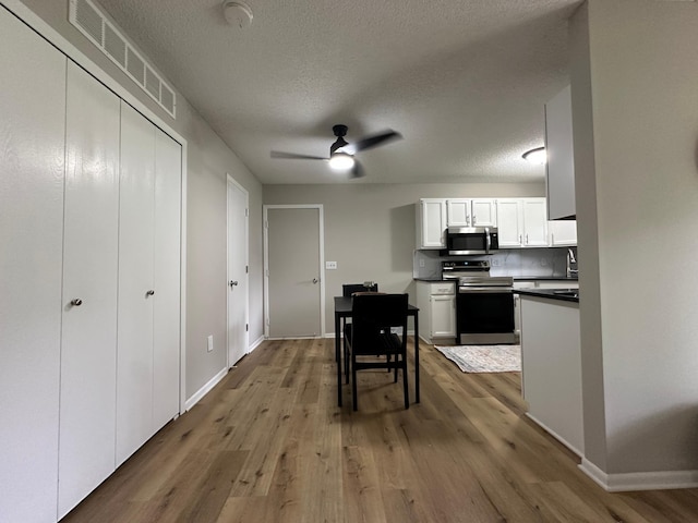 12619 Alder St NW, Coon Rapids, MN 55448 - kitchen with stainless steel appliances, wood finished floors, dark countertops, white cabinetry, and a textured ceiling