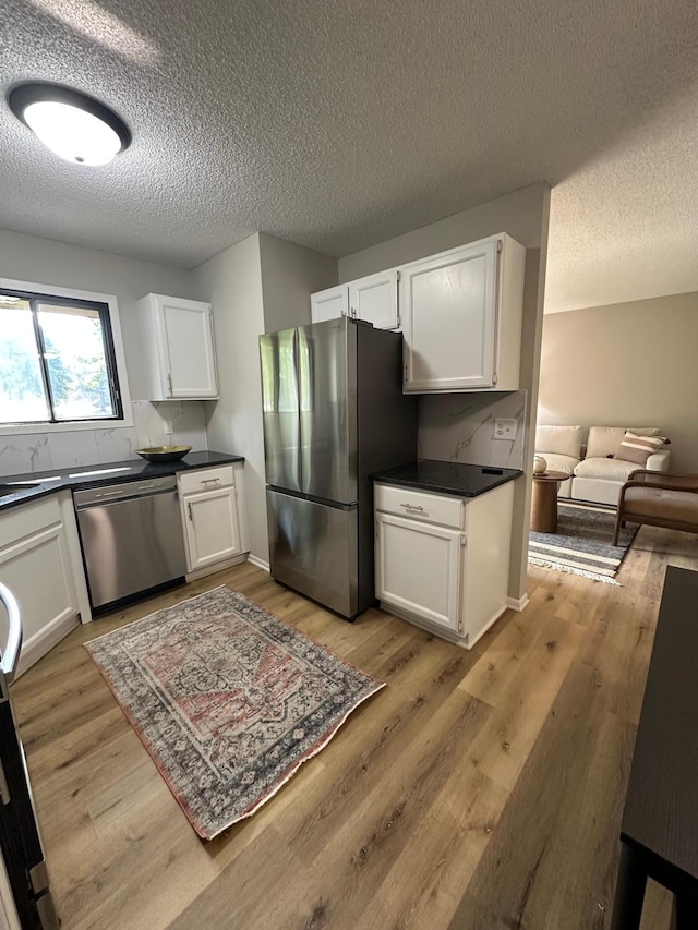 12619 Alder St NW, Coon Rapids, MN 55448 - kitchen featuring appliances with stainless steel finishes, a textured ceiling, dark countertops, white cabinetry, and light wood-type flooring