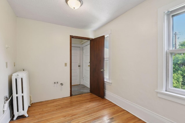 1108 16th Ave SE, Minneapolis, MN 55414 - empty room with radiator heating unit, plenty of natural light, light wood-style floors, and a textured ceiling
