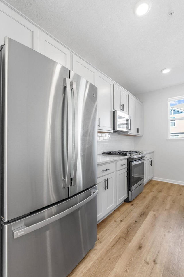 7614 Connie Ln, Inver Grove Heights, MN 55076 - kitchen featuring stainless steel appliances, light wood finished floors, white cabinets, tasteful backsplash, and light countertops