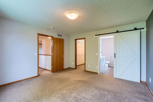 2907 Asarum Ct, Shakopee, MN 55379 - unfurnished bedroom featuring a spacious closet, carpet flooring, a textured ceiling, connected bathroom, and a barn door