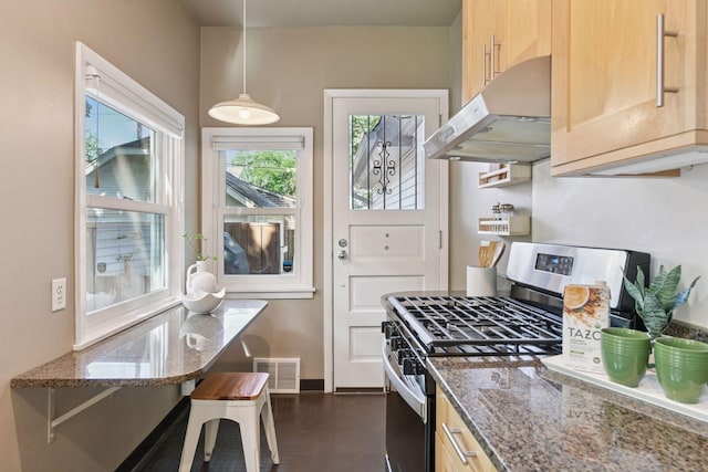 2432 Pleasant Ave, Minneapolis, MN 55404 - kitchen with stainless steel gas range, under cabinet range hood, dark stone countertops, decorative light fixtures, and light brown cabinetry