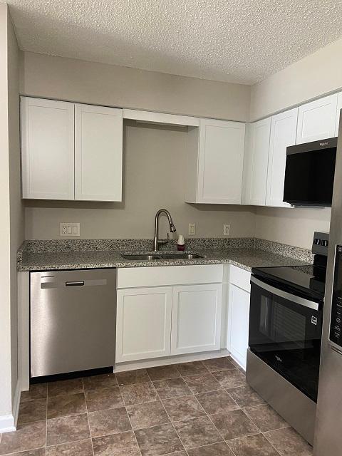 1340 119th Ln NW, Coon Rapids, MN 55448 - kitchen with appliances with stainless steel finishes, white cabinets, a textured ceiling, and dark stone counters