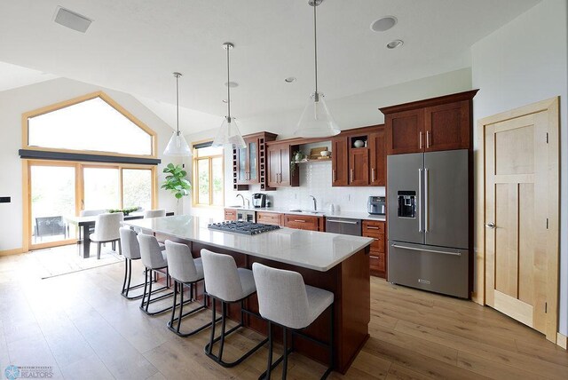 4703 Woodhaven St S, Fargo, ND 58104 - kitchen with stainless steel appliances, a kitchen island, a kitchen breakfast bar, light wood-style flooring, and backsplash