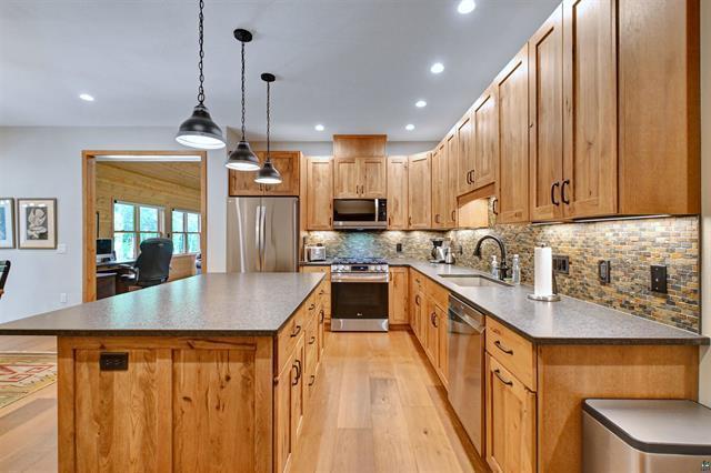 12207 Railroad Rd, Lake Nebagamon, WI 54849 - kitchen featuring appliances with stainless steel finishes, light wood-style floors, a center island, decorative backsplash, and decorative light fixtures