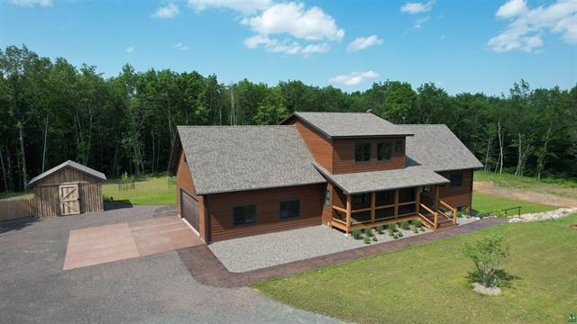 12207 Railroad Rd, Lake Nebagamon, WI 54849 - rustic home featuring a garage, a view of trees, a front yard, a storage shed, and driveway