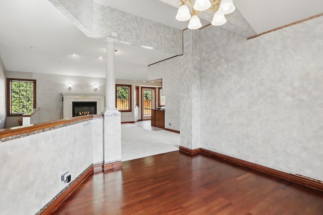 11228 River Rd, Champlin, MN 55316 - unfurnished living room featuring wood finished floors, a chandelier, a warm lit fireplace, and decorative columns
