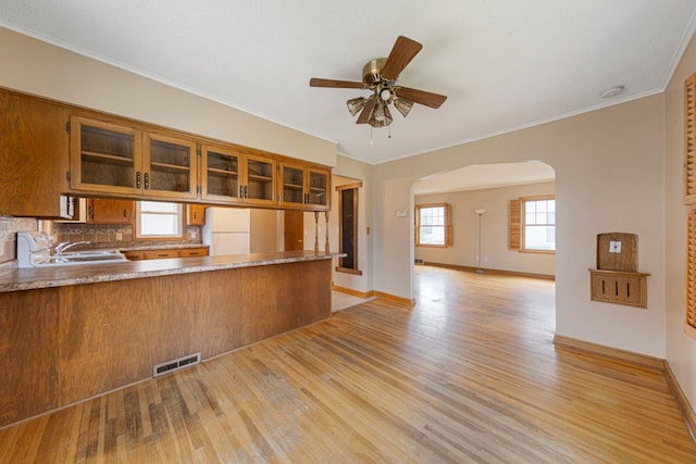 215 Plainview St, Owatonna, MN 55060 - kitchen featuring arched walkways, light wood finished floors, brown cabinets, ceiling fan, and glass insert cabinets