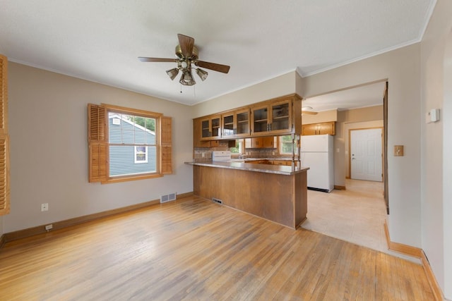 215 Plainview St, Owatonna, MN 55060 - kitchen featuring freestanding refrigerator, a peninsula, brown cabinets, glass insert cabinets, and a ceiling fan