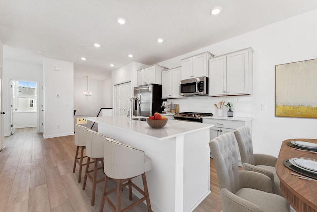 2700 Kepler Ave NE, Saint Michael, MN 55376 - kitchen with stainless steel appliances, a kitchen bar, an island with sink, tasteful backsplash, and light wood finished floors