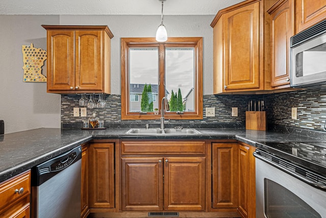 133 Uriah Ct, Mankato, MN 56001 - kitchen featuring stainless steel appliances, decorative backsplash, dark countertops, brown cabinets, and hanging light fixtures