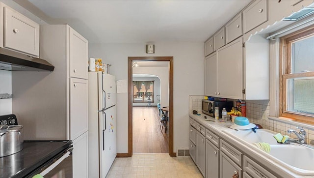 806 8th St SW, Willmar, MN 56201 - kitchen with appliances with stainless steel finishes, under cabinet range hood, light countertops, backsplash, and arched walkways