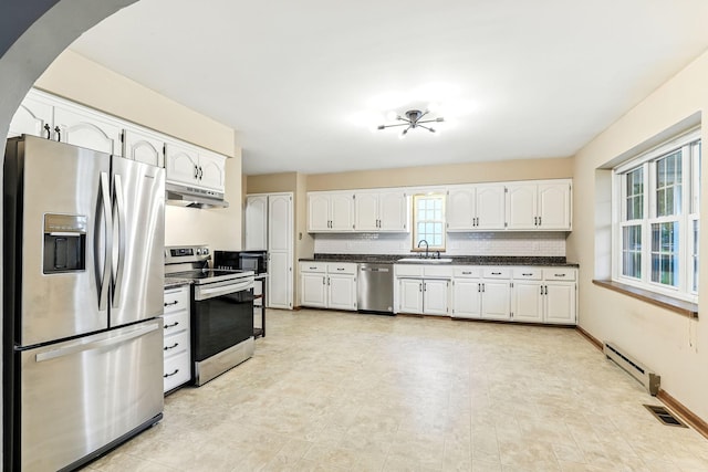 453 Van Dyke St, Saint Paul, MN 55119 - kitchen with stainless steel appliances, under cabinet range hood, dark countertops, a baseboard radiator, and white cabinetry