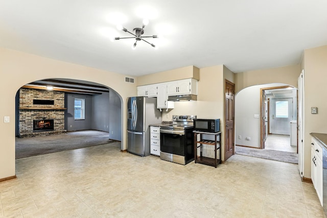 453 Van Dyke St, Saint Paul, MN 55119 - kitchen with appliances with stainless steel finishes, arched walkways, white cabinets, a fireplace, and light colored carpet