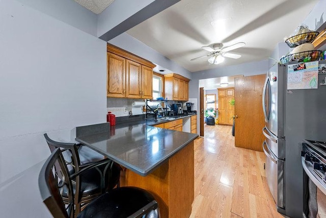 2813 Ohenry Rd, Brooklyn Center, MN 55430 - kitchen featuring stainless steel appliances, brown cabinetry, dark countertops, light wood-style flooring, and a peninsula