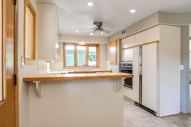 3330 Belden Dr NE, Saint Anthony, MN 55418 - kitchen featuring black oven, freestanding refrigerator, a peninsula, a ceiling fan, and white cabinetry