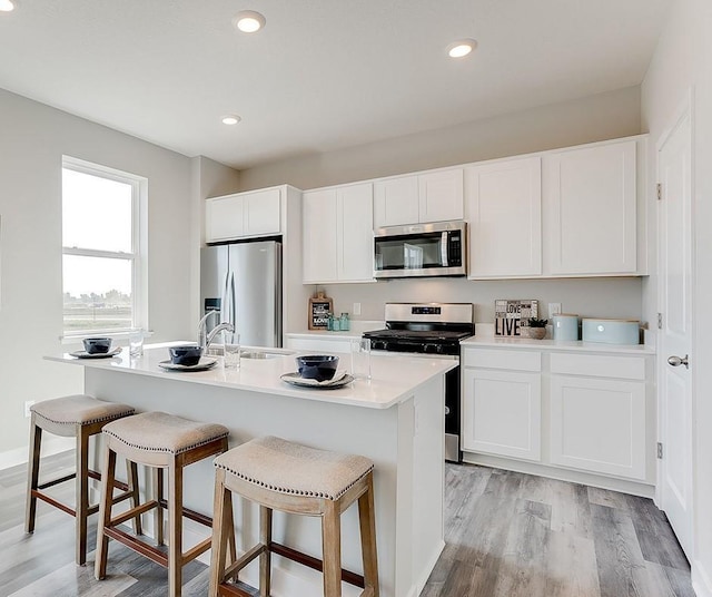 927 Redfield Cir, Delano, MN 55328 - kitchen featuring appliances with stainless steel finishes, white cabinetry, light wood-style floors, a kitchen island with sink, and recessed lighting