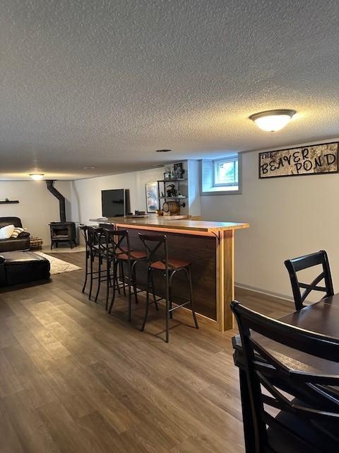 5025 Wilshire Blvd, Crystal, MN 55429 - indoor bar featuring a wood stove, a textured ceiling, and light wood-style flooring