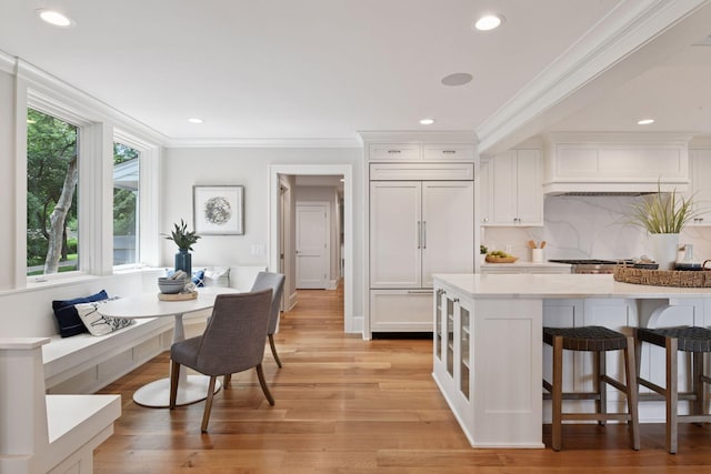 2462 Lafayette Rd, Minnetonka Beach, MN 55391 - kitchen with custom exhaust hood, white cabinets, decorative backsplash, a kitchen breakfast bar, and crown molding