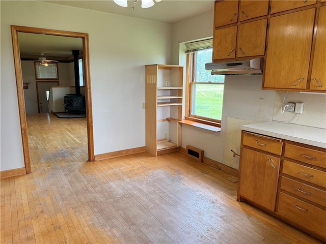 2999 18th St, Oak Grove Twp, WI 54868 - kitchen with under cabinet range hood, a wood stove, light wood-style floors, brown cabinetry, and ceiling fan