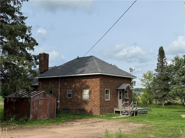 2999 18th St, Oak Grove Twp, WI 54868 - rear view of house featuring a storage unit, a chimney, brick siding, a shingled roof, and a yard