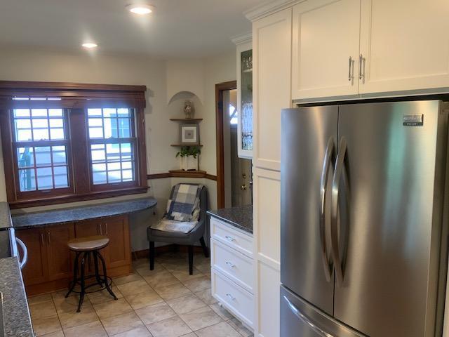 5504 Elliot Ave, Minneapolis, MN 55417 - kitchen featuring freestanding refrigerator, white cabinetry, dark stone countertops, light tile patterned floors, and glass insert cabinets