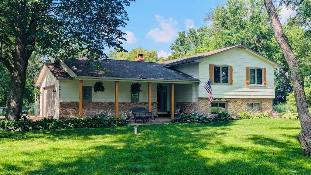 19720 Jackie Ln, Corcoran, MN 55374 - split level home with brick siding, a front yard, a chimney, and covered porch