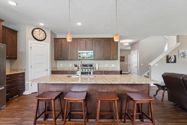 24000 Helium Ct, Forest Lake, MN 55025 - kitchen with a textured ceiling, dark wood-style flooring, a breakfast bar area, a kitchen island with sink, and light stone countertops