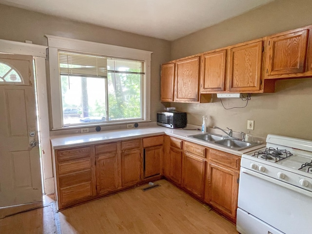 629 Farrington St, Saint Paul, MN 55103 - kitchen with white range with gas cooktop, light countertops, light wood-type flooring, stainless steel microwave, and brown cabinetry