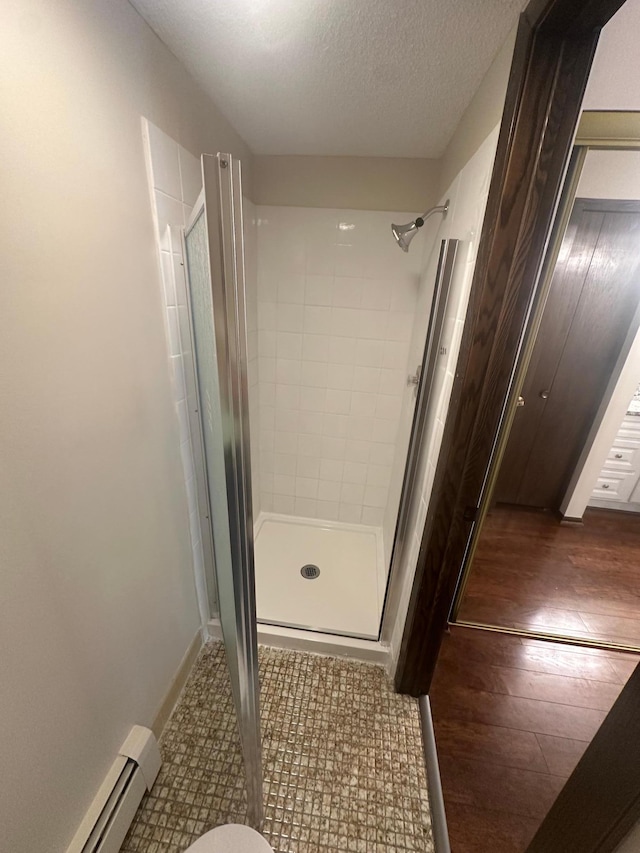 2485 Londin Ln E Unit 418, Maplewood, MN 55119 - bathroom featuring baseboard heating, a shower stall, a textured ceiling, and wood finished floors