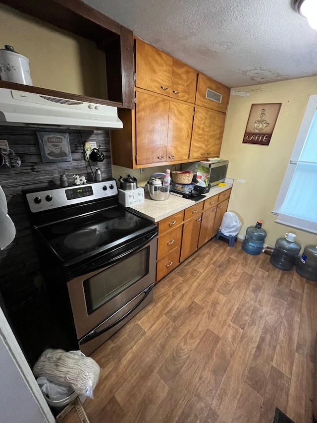102 4th St S, Grove City, MN 56243 - kitchen with stainless steel range with electric stovetop, light wood-style floors, brown cabinets, under cabinet range hood, and a textured ceiling