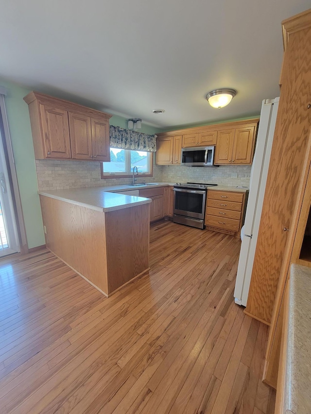 619 3rd St NW, Forest Lake, MN 55025 - kitchen with appliances with stainless steel finishes, light wood-style flooring, a peninsula, and backsplash
