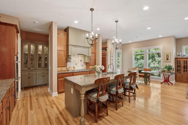 17244 Valley Rd, Eden Prairie, MN 55347 - kitchen featuring light wood-type flooring, a kitchen island with sink, light stone countertops, brown cabinetry, and a breakfast bar area