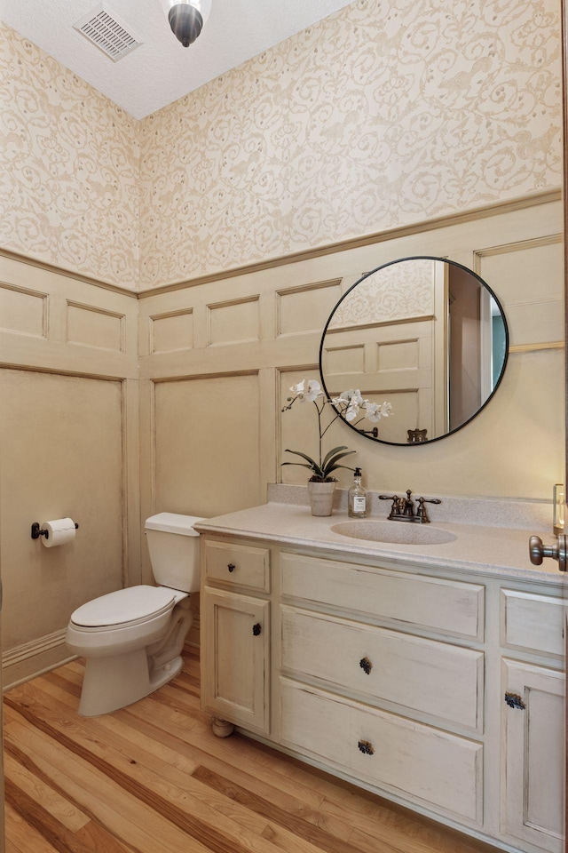 17244 Valley Rd, Eden Prairie, MN 55347 - half bathroom featuring a decorative wall, wallpapered walls, vanity, wainscoting, and wood finished floors