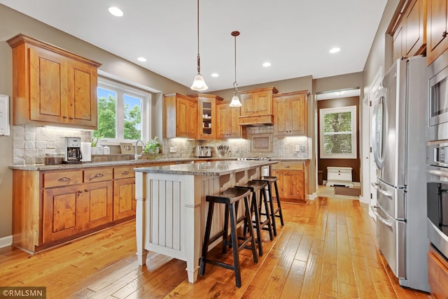 3631 Woodcrest Cir, Eagan, MN 55123 - kitchen featuring appliances with stainless steel finishes, a center island, light wood finished floors, a breakfast bar, and backsplash