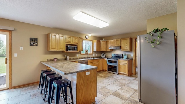1902 11th Ave NE, Kasson, MN 55944 - kitchen with appliances with stainless steel finishes, a peninsula, a kitchen bar, a textured ceiling, and under cabinet range hood