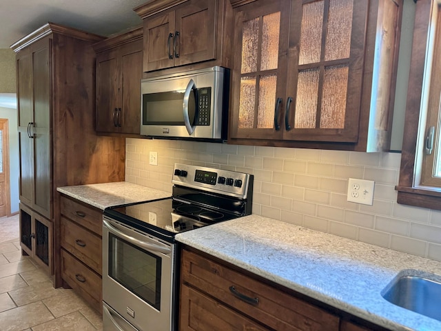 90760 US Highway 71, Christiania Twp, MN 56101 - kitchen featuring appliances with stainless steel finishes, decorative backsplash, light stone counters, dark brown cabinets, and glass insert cabinets