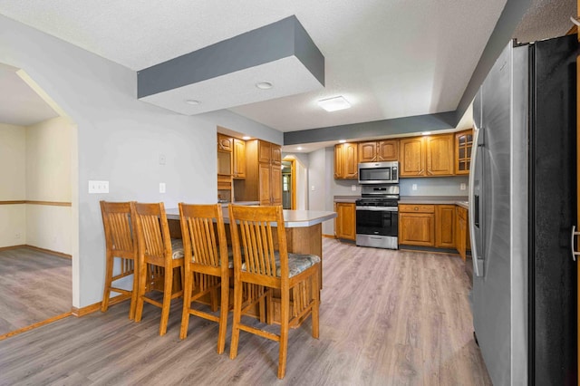 51800 500th St, Menahga, MN 56464 - kitchen featuring stainless steel appliances, brown cabinets, light wood finished floors, a breakfast bar area, and light countertops
