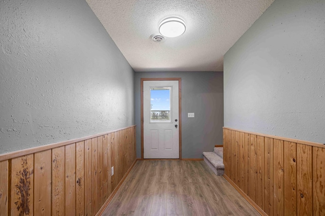 51800 500th St, Menahga, MN 56464 - doorway to outside featuring wooden walls, a textured ceiling, light wood-style floors, stairs, and a wainscoted wall