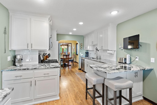 10315 Boundary Creek Ter, Maple Grove, MN 55369 - kitchen with white cabinetry, arched walkways, tasteful backsplash, light wood-type flooring, and recessed lighting
