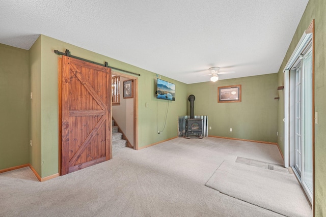24864 Kettle River Blvd, Wyoming, MN 55025 - carpeted empty room featuring a wood stove, a barn door, a textured ceiling, a ceiling fan, and stairway