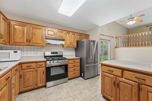 24864 Kettle River Blvd, Wyoming, MN 55025 - kitchen featuring appliances with stainless steel finishes, light countertops, under cabinet range hood, backsplash, and brown cabinetry