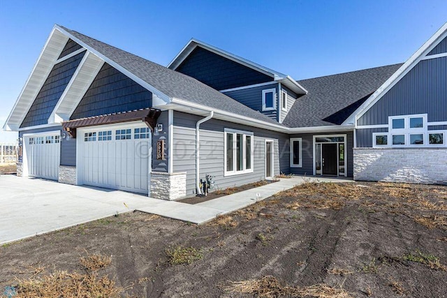 craftsman-style home featuring a garage, stone siding, driveway, and a shingled roof