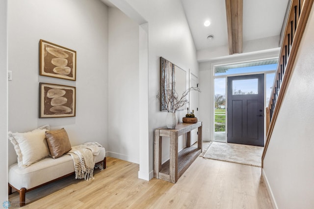 foyer entrance featuring beamed ceiling, a towering ceiling, and light wood-type flooring