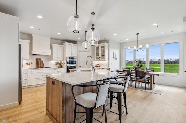 kitchen with white cabinetry, a center island with sink, light wood-type flooring, and custom exhaust hood