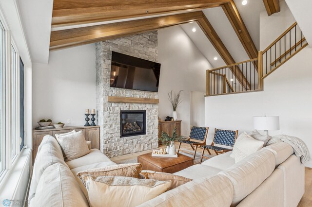 living room with hardwood / wood-style floors, beam ceiling, a stone fireplace, and high vaulted ceiling