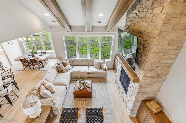 living room with beamed ceiling, a notable chandelier, a stone fireplace, and light wood-type flooring